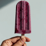 A hand holding a single, creamy Blueberry, Thyme and Sweet Cream Ice Pop.