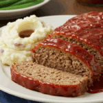 A classic dinner plate with a thick slice of Classic Meatloaf, mashed potatoes, and green beans.