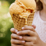 A child happily holding a large waffle cone of homemade Peach Ice Cream on a sunny summer day.