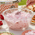 Serving a scoop of Cherry Fluff from a large bowl at a summer potluck.