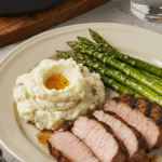 A plated meal of a Grilled Pork Chop with mashed potatoes and asparagus.