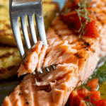 A fork flaking a piece of the juicy, finished Grilled Salmon.