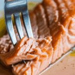 A fork flaking a piece of the juicy, finished Pan-Seared Salmon.