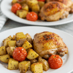 A plated meal of roasted chicken with a side of Roasted Potatoes and Tomatoes.