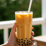 A person's hands holding a refreshing, cold glass of homemade Thai Milk Tea Boba on a sunny day.