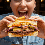 A person taking a big, happy bite of a crunchy Cuban Beef-and-Potato Sandwich.