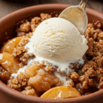 A close-up of a warm bowl of Old-Fashioned Apple Crisp with a scoop of vanilla ice cream melting on top.