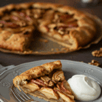 An elegant slice of homemade Apple-Walnut Galette being served with a quenelle of mascarpone at a dinner party.