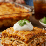 A perfect, layered slice of homemade Chicken Enchilada Casserole topped with sour cream, being served for a family dinner.