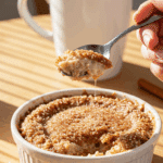 A spoon cracking the crispy churro topping of a warm bowl of baked oats.
