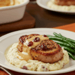A beautiful plate of homemade Cranberry-Stuffed Pork Chops and cream sauce, served over a bed of creamy mashed potatoes.