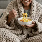 A person wrapped in a cozy blanket, happily eating a warm, steaming bowl of homemade Creamy Chicken Noodle Soup.