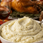 A large, beautiful bowl of Creamy Garlic Mashed Potatoes being served as a side dish at a festive holiday dinner.