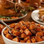 A beautiful bowl of Honey-Roasted Sweet Potatoes being served as a side dish at a festive Thanksgiving dinner.