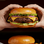 A person's hands holding a large, delicious Juicy Lucy burger, ready to take the first bite.