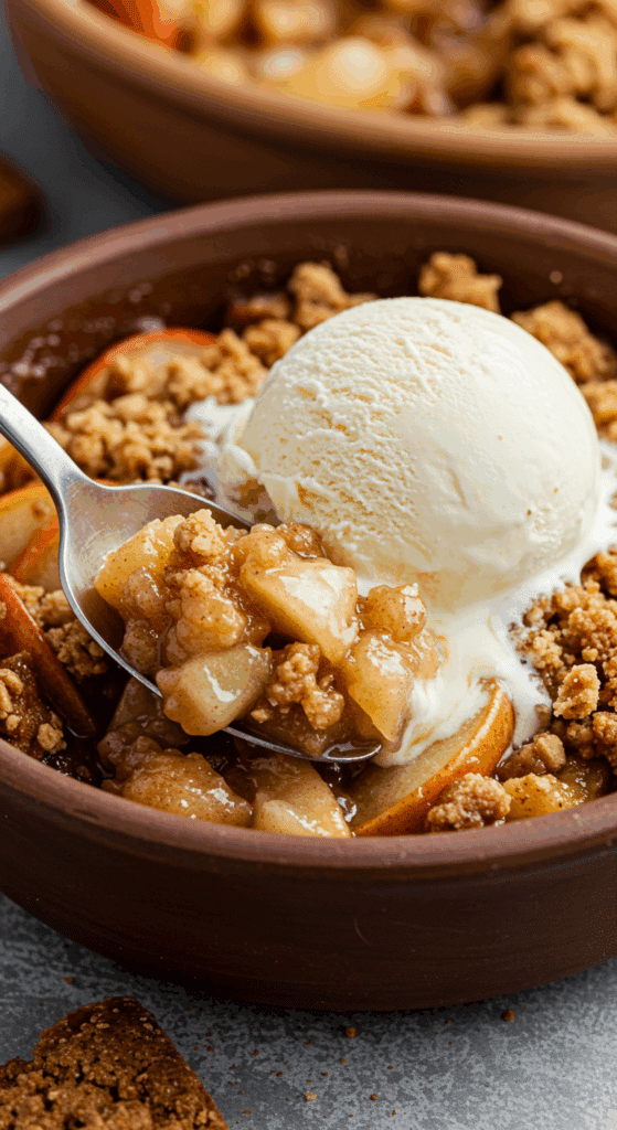 A close-up of a warm bowl of Apple and Pear Crisp with a scoop of vanilla ice cream melting on top.