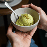 A person's hands holding a beautiful bowl with a single scoop of homemade Pistachio Ice Cream.