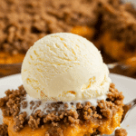 A warm, cozy bowl of homemade Pumpkin Dump Cake with a large scoop of melting vanilla ice cream on top.
