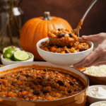 A large pot of homemade Pumpkin Chili Verde being served at a fun fall party with a toppings bar.