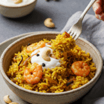 A cozy bowl of homemade Sheet Pan Shrimp Biryani, topped with yogurt and cashews, being served for an easy dinner.