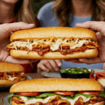 A hand holding a large, delicious, and messy homemade Chicken Cacciatore Sub at a fun game day party.