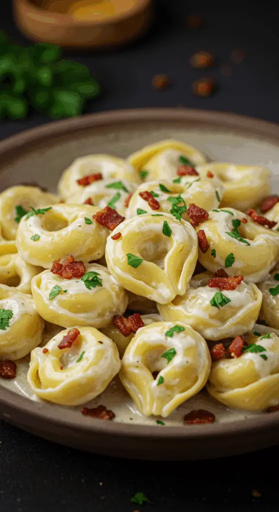 A beautiful, rustic bowl of homemade, creamy Tortellini Carbonara, with crispy bacon and fresh parsley.