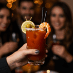A hand holding an elegant glass of a homemade, spicy Bloody Mary Shrimp Cocktail at a fun and sophisticated holiday party.