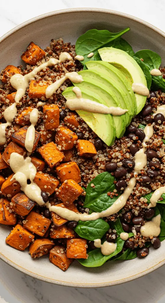 A beautiful, overhead shot of a homemade, healthy, and colorful Roasted Sweet Potato, Black Bean, and Quinoa Salad in a large serving bowl, drizzled with a creamy tahini dressing.