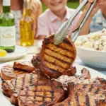 A large platter of homemade, juicy Grilled Pork Chops being served at a fun summer barbecue.