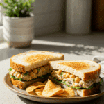 A beautiful plate of a homemade, healthy Chickpea Salad Sandwich being enjoyed with a side of crispy potato chips for a vibrant and healthy lunch.