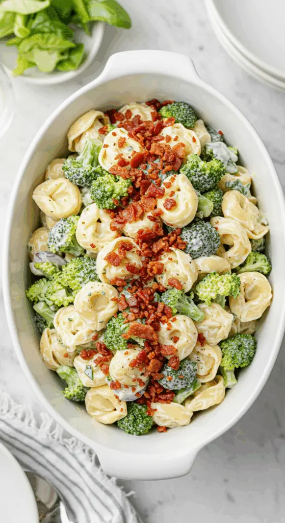 A beautiful, large serving bowl of homemade, creamy Tortellini Salad with broccoli and a generous topping of crispy, crumbled bacon.