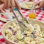 A large bowl of homemade, creamy Tortellini Salad being served at a fun summer picnic.