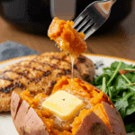 A beautiful plate of a homemade, elegant, and crispy Air Fryer Sweet Potato, being served with a grilled chicken breast and a green salad for a healthy dinner.