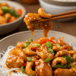 A cozy bowl of homemade, saucy Spicy Cashew Chicken being served over noodles for a casual family dinner.