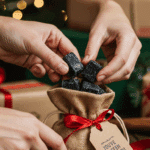 A pair of hands carefully placing beautiful, rustic, black lumps of a homemade Christmas Coal Candy into a small burlap drawstring bag as a homemade Christmas gift.