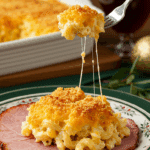 A beautiful plate of a homemade, elegant, and crispy-topped Baked Mac and Cheese, being served with a thick slice of a glazed ham at a holiday dinner.