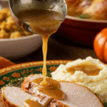 A beautiful plate of a homemade, elegant, and rich Classic Turkey Gravy, being poured over thick slices of a roasted turkey at a Thanksgiving dinner.
