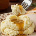 A beautiful plate of a homemade, elegant, and silky-smooth Garlic Mashed Potatoes, being served with a thick slice of a roasted turkey and gravy at a Thanksgiving dinner.