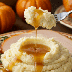 A beautiful plate of a homemade, elegant, and silky-smooth Garlic Mashed Potatoes, being served with a thick slice of a roasted turkey and gravy at a Thanksgiving dinner.