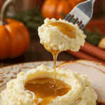 A beautiful plate of a homemade, elegant, and golden-topped Creamy Mashed Potatoes, being served with a thick slice of a roasted turkey and gravy at a Thanksgiving dinner.