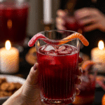 A hand holding an elegant glass of a homemade, red, and spooky "Haunted" Hibiscus Punch at a fun and festive Halloween party.