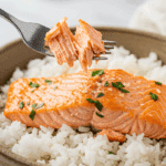 A cozy bowl of homemade, moist Microwave Salmon in a red curry sauce being enjoyed with a fork for a casual, healthy dinner.