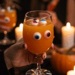 A hand holding an elegant glass of a homemade, orange, and spooky "Monster Melon" Punch at a fun and festive Halloween party.