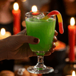 A hand holding an elegant glass of a homemade, green, and spooky "Mummy's Brew" Punch at a fun and festive Halloween party.