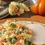 A beautiful plate of a homemade, elegant, and vibrant Thanksgiving Pasta Salad, being served with a thick slice of a roasted turkey at a Thanksgiving dinner.