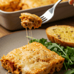 A beautiful, cheesy slice of homemade Vegan Pasta Bake being served with a side of salad and garlic bread for a family dinner.