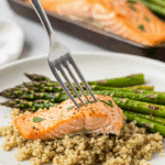 A healthy dinner plate with a serving of homemade, saucy Sheet Pan Salmon and Asparagus, served over a bed of quinoa for a cozy meal.