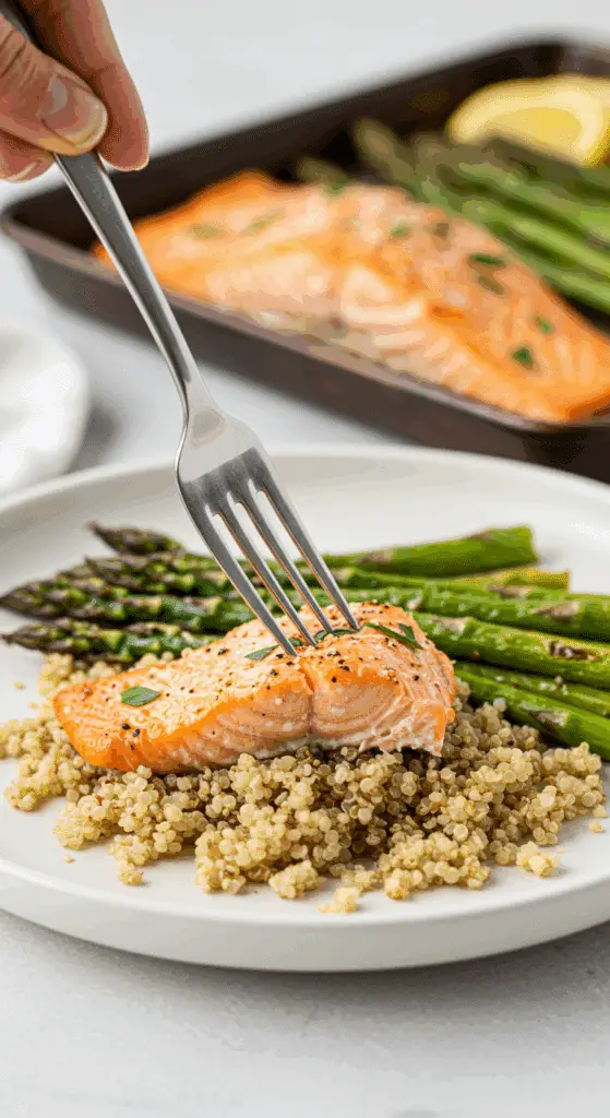 A healthy dinner plate with a serving of homemade, saucy Sheet Pan Salmon and Asparagus, served over a bed of quinoa for a cozy meal.