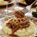 A beautiful plate of a homemade, elegant, and shredded French Onion Pot Roast, being served over creamy mashed potatoes at a Sunday dinner.