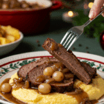 A beautiful plate of a homemade, elegant, and sliced Onion-Braised Brisket, being served over creamy polenta at a holiday dinner.